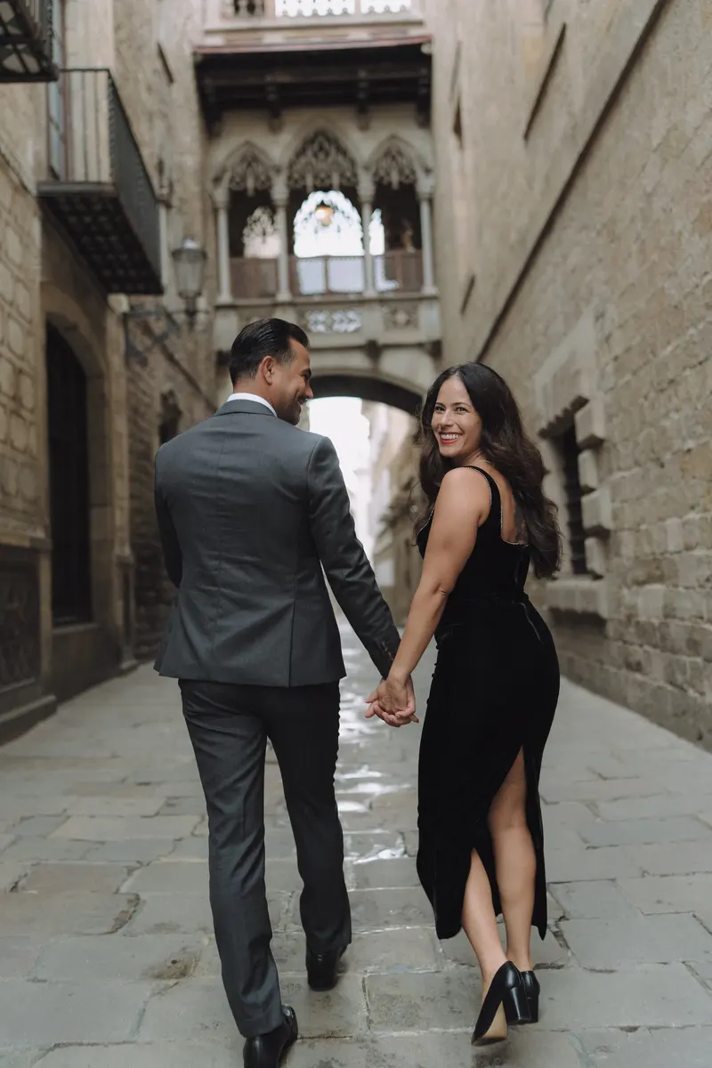 Ashley and Edgar walk away together along the narrow street beneath Pont del Bisbe.