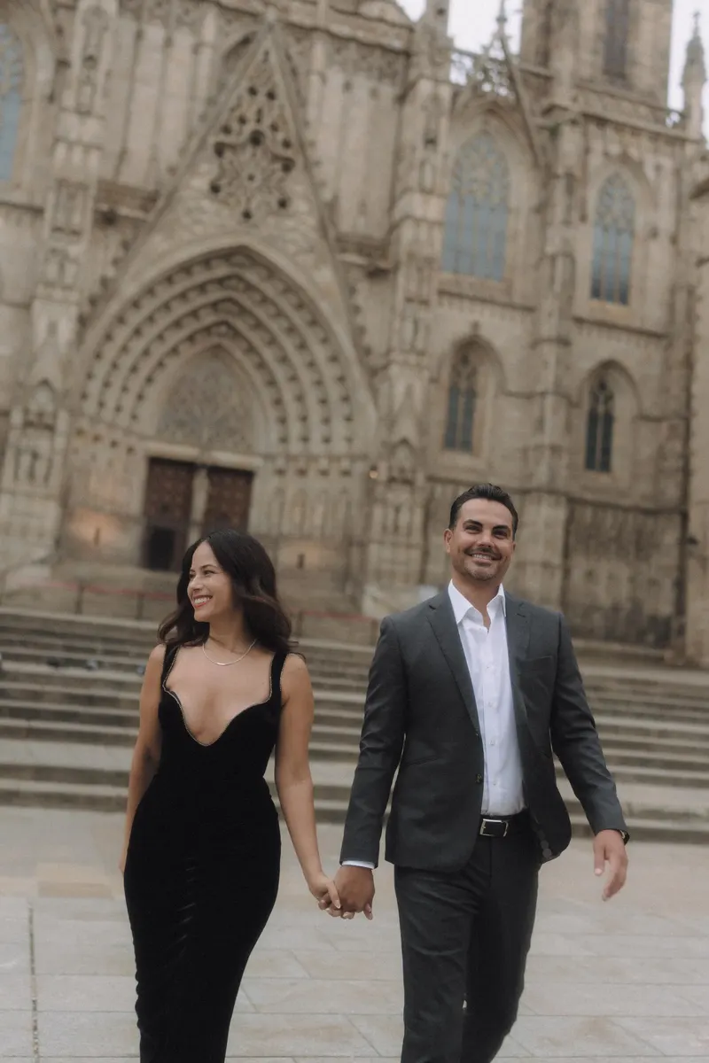 Ashley and Edgar walk hand in hand across the cathedral square in elegant black outfits.