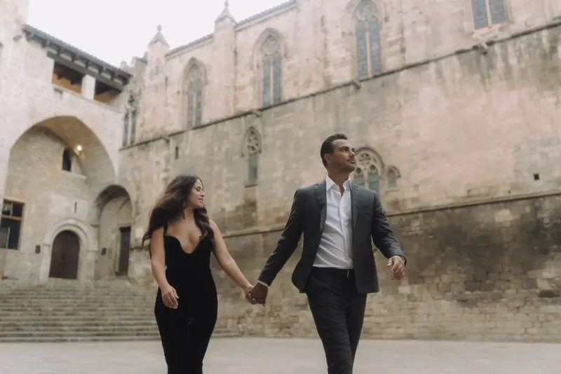 Ashley and Edgar walk hand in hand through the spacious medieval square of Plaça del Rei.