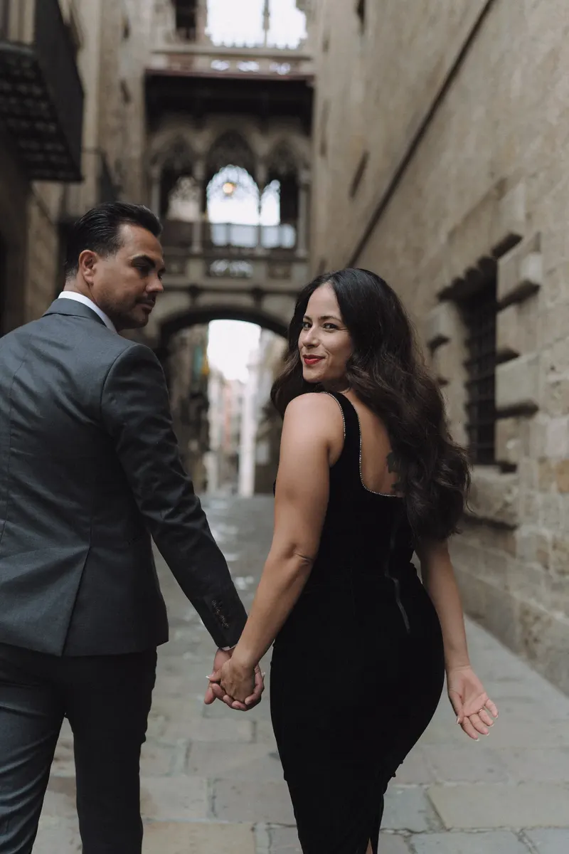 Ashley looks over her shoulder as she walks hand in hand with Edgar beneath Pont del Bisbe.