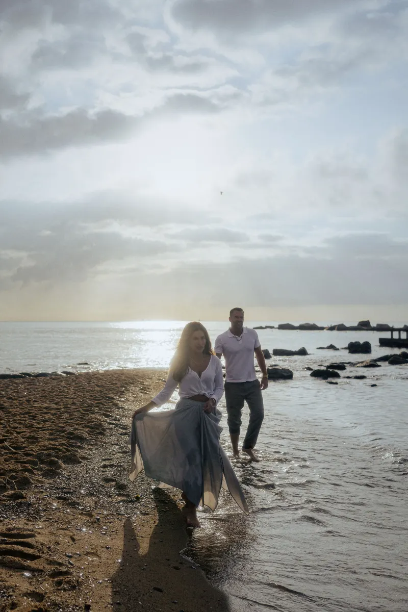 Barefoot couple strolling along the shoreline at sunset, captured during a couples & engagements photoshoot.