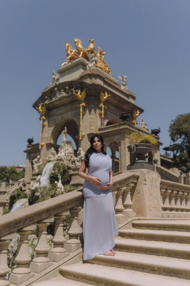 Barefoot expectant mother in a soft blue dress poses on grand steps at Parc de la Ciutadella, Vacation Portraits session.