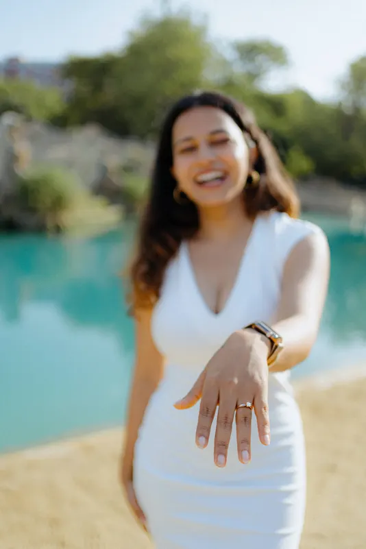Beaming with joy, a newly engaged woman shows off her ring during a surprise proposal photoshoot by the water.