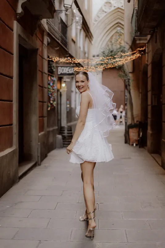 Bride-to-be in a short white dress and veil smiles while strolling down a charming Barcelona street, Vacation Portraits sessi