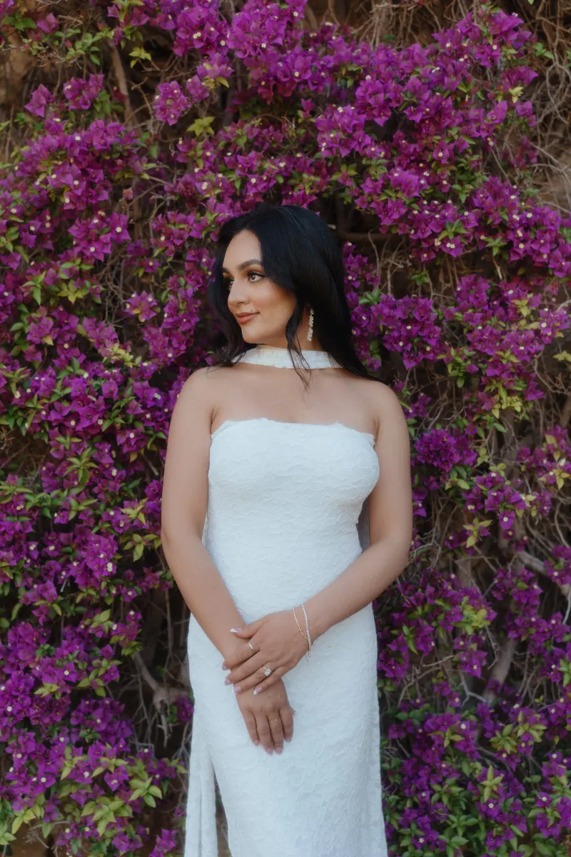Bride-to-be in a white lace dress stands before blooming bougainvillea, captured during a surprise proposal session.