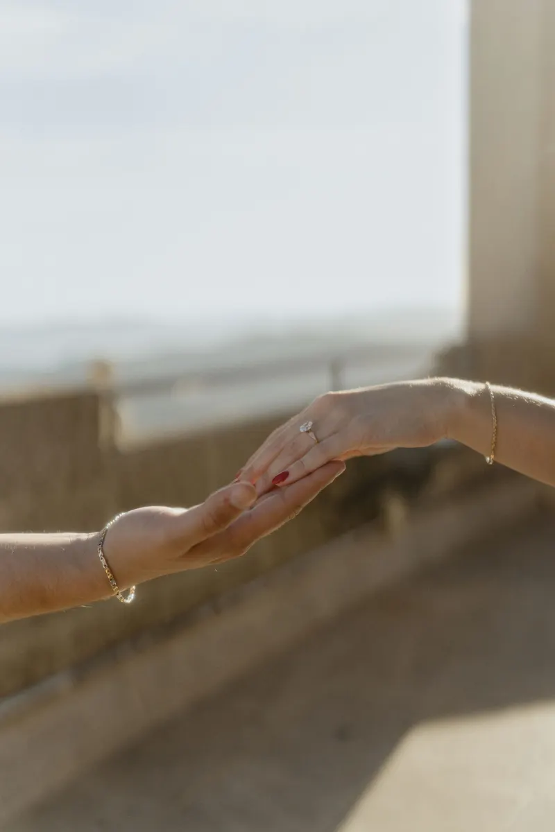 Close-up of a couple gently touching hands, her engagement ring sparkling in golden light during an engagement session.