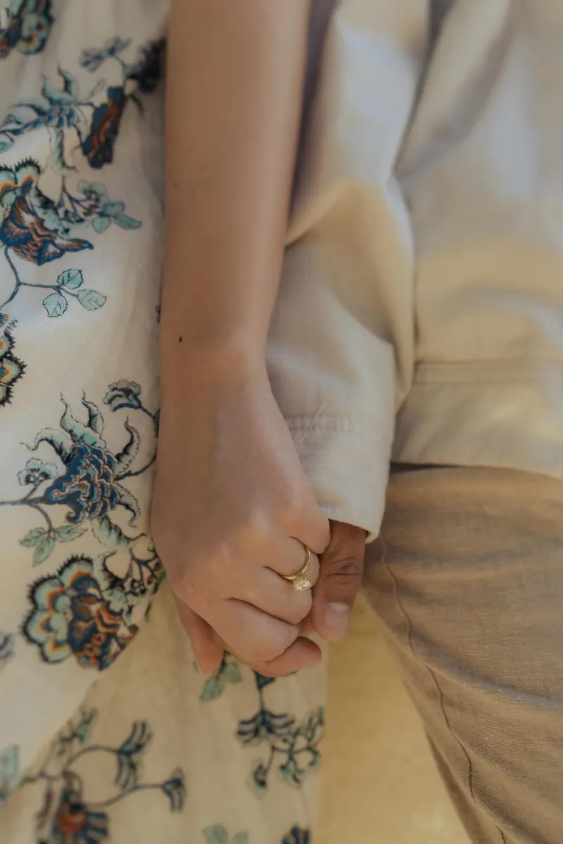 Close-up of a couple holding hands, engagement ring visible, captured during a surprise proposal photoshoot by the sea.