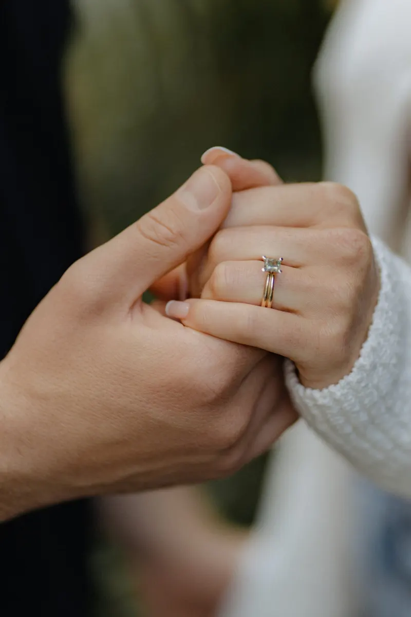 Close-up of a couple holding hands, her engagement ring sparkling during a couples & engagements photoshoot outdoors.