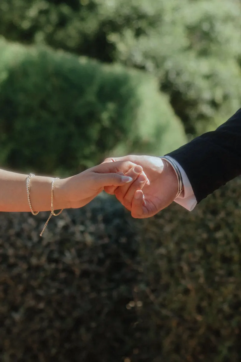 Close-up of a couple holding hands in a sunlit Begur garden, capturing a tender moment from a surprise proposal session.