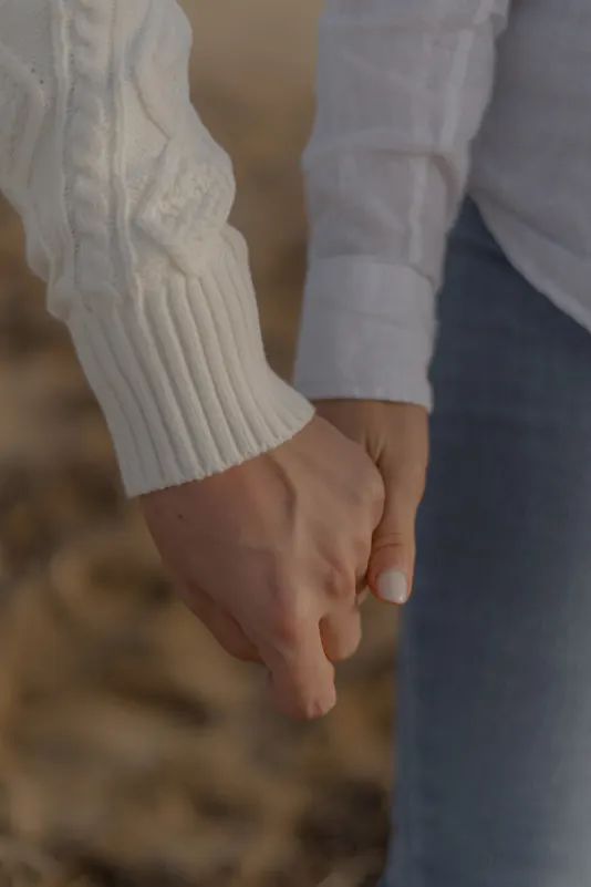 Close-up of a couple holding hands on the sand, capturing a tender moment during a couples & engagements shoot in Barcelona.