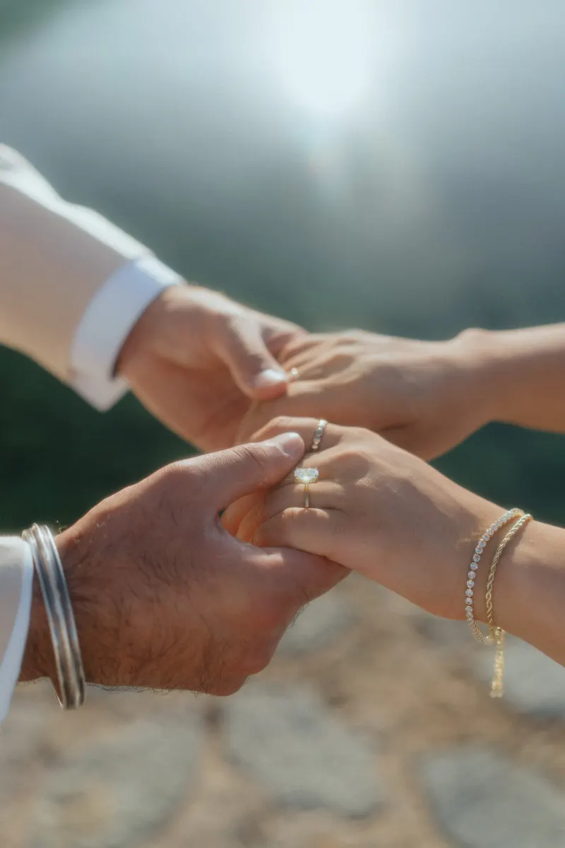 Close-up of a couple holding hands outdoors, capturing the emotional moment of a surprise proposal photoshoot.