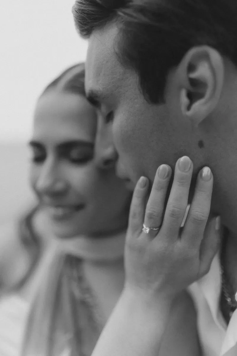 Close-up of a couple sharing an intimate moment, her hand with an engagement ring gently touching his face.