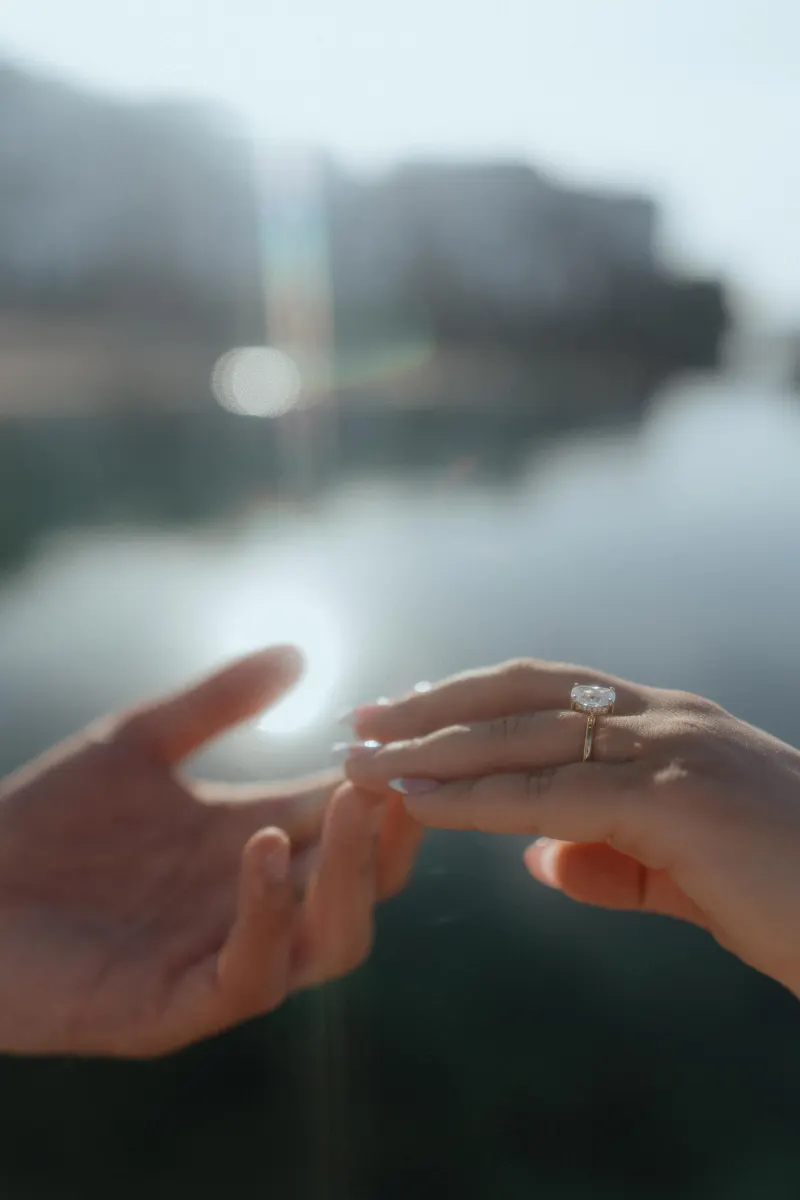 Close-up of a couple’s hands as an engagement ring is placed during a surprise proposal photoshoot by the water.