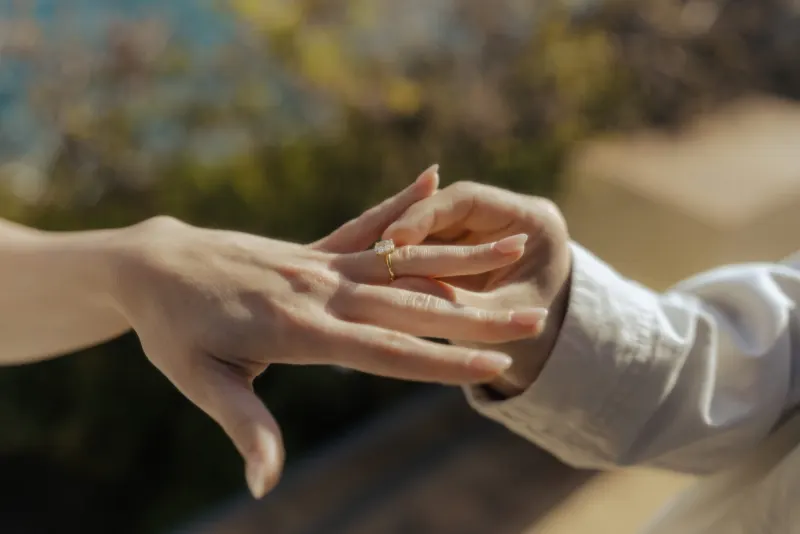 Close-up of a couple’s hands as he gently slides an engagement ring on her finger during a seaside proposal photoshoot.