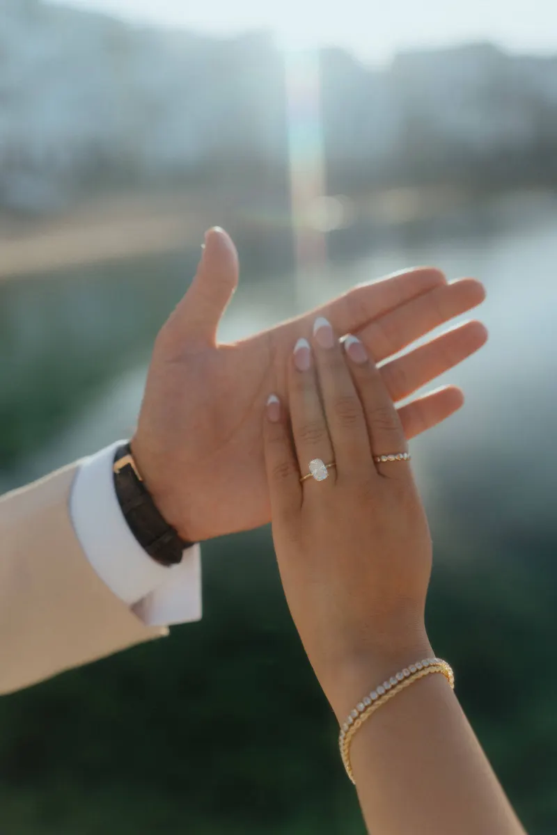 Close-up of a couple’s hands, showing an engagement ring during a surprise proposal photoshoot by the water.