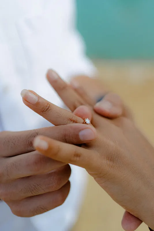 Close-up of a diamond ring being placed on a finger during a surprise proposal photoshoot.