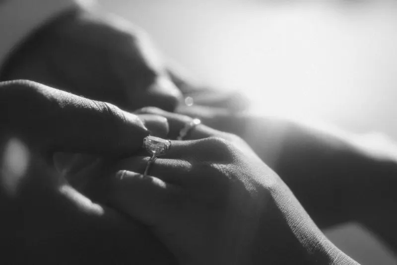 Close-up of a hand slipping an engagement ring onto a finger, capturing a tender surprise proposal moment.