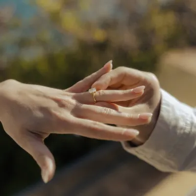 Close-up of a hand slipping an engagement ring onto a finger during a romantic surprise proposal photoshoot outdoors.