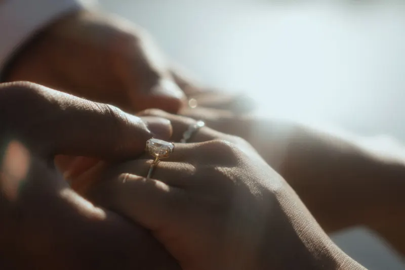 Close-up of a hand slipping an engagement ring onto a finger during a surprise proposal photoshoot.