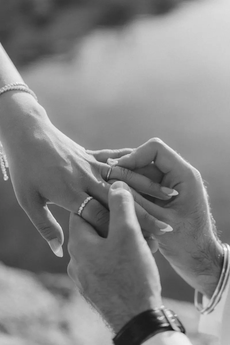 Close-up of a man placing an engagement ring on his partner’s finger during a surprise proposal photoshoot outdoors.