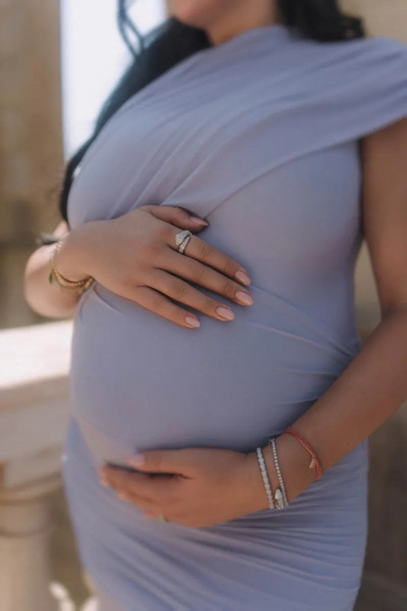 Close-up of a pregnant woman in a lilac dress cradling her belly, Vacation Portraits session in Barcelona.
