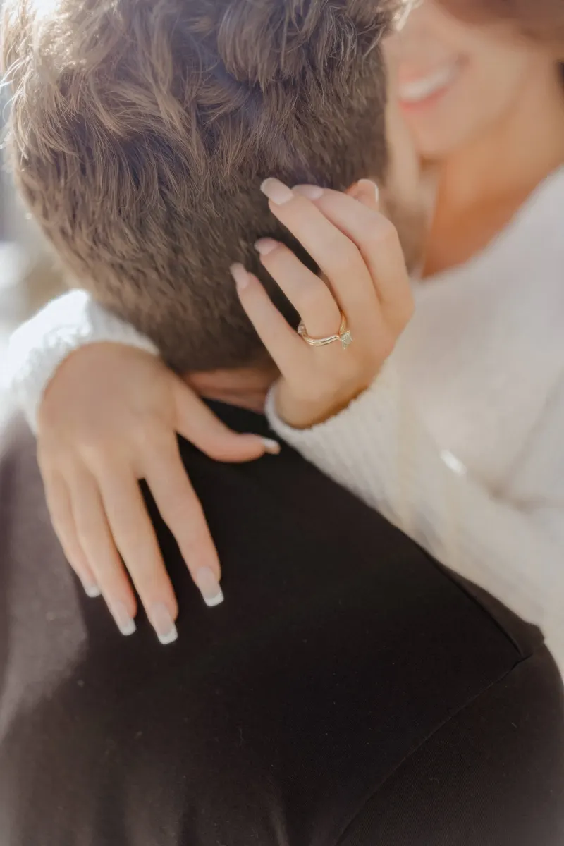Close-up of a smiling woman embracing her partner, her engagement ring catching the light during a couples photoshoot.