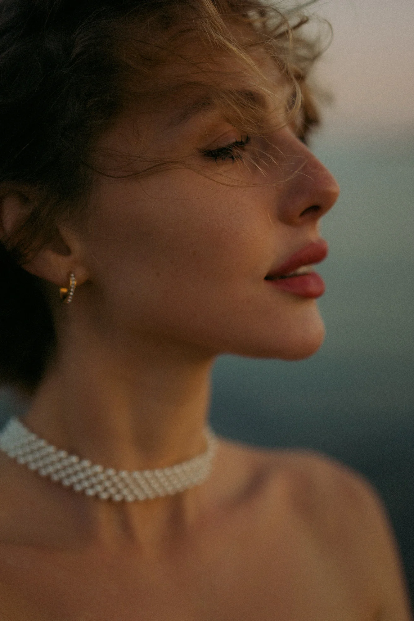Close-up of a woman with eyes closed, enjoying a peaceful seaside breeze during a Vacation Portraits photoshoot at sunset.