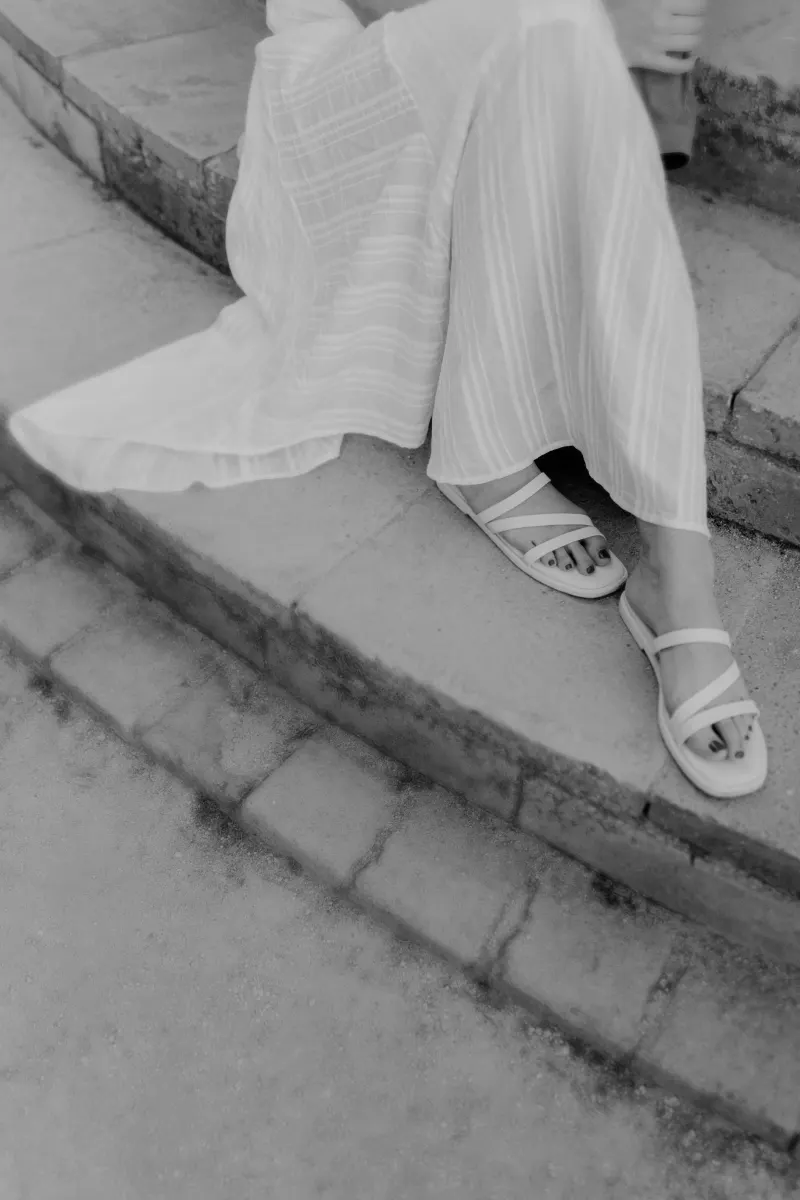 Close-up of a woman’s flowing dress and sandals as she sits on stone steps during a couples & engagements session.