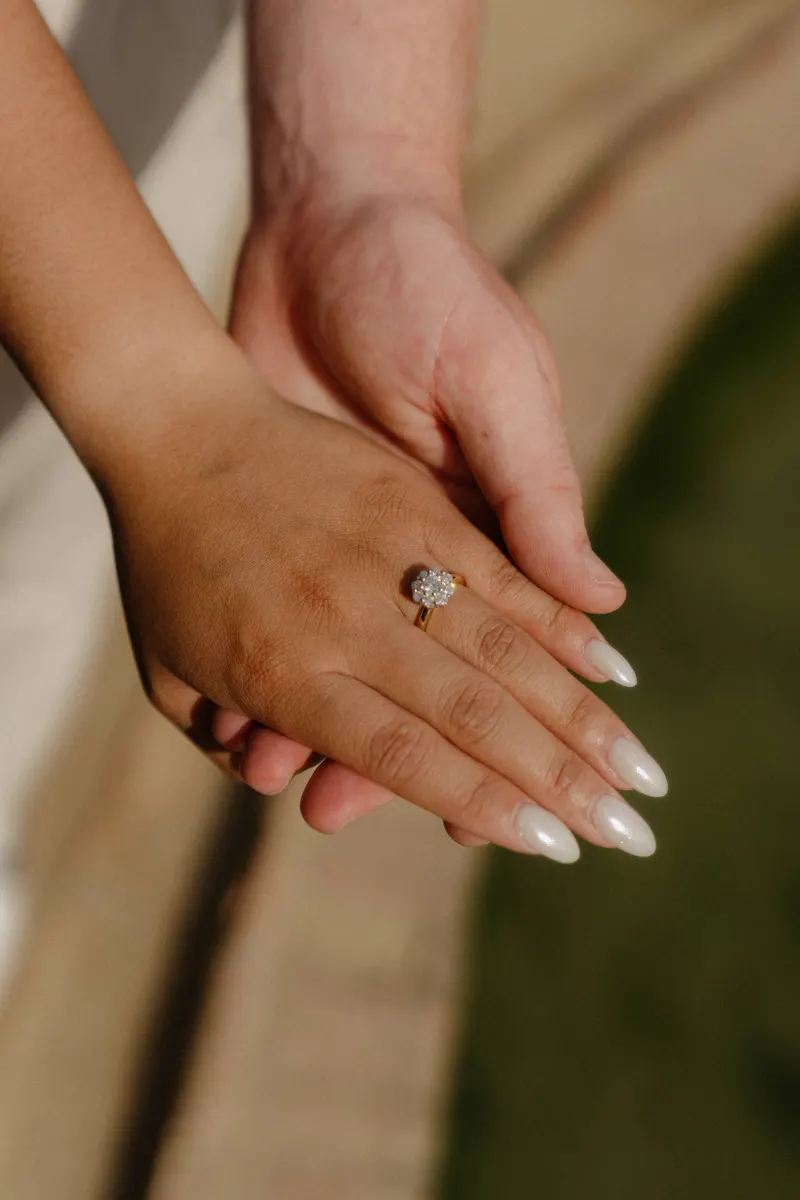 Close-up of couple’s hands highlighting an engagement ring, captured during a surprise proposal photoshoot in the garden.