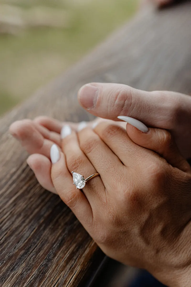 Close-up of newly engaged couple holding hands, showcasing her pear-shaped ring after a surprise proposal photoshoot.