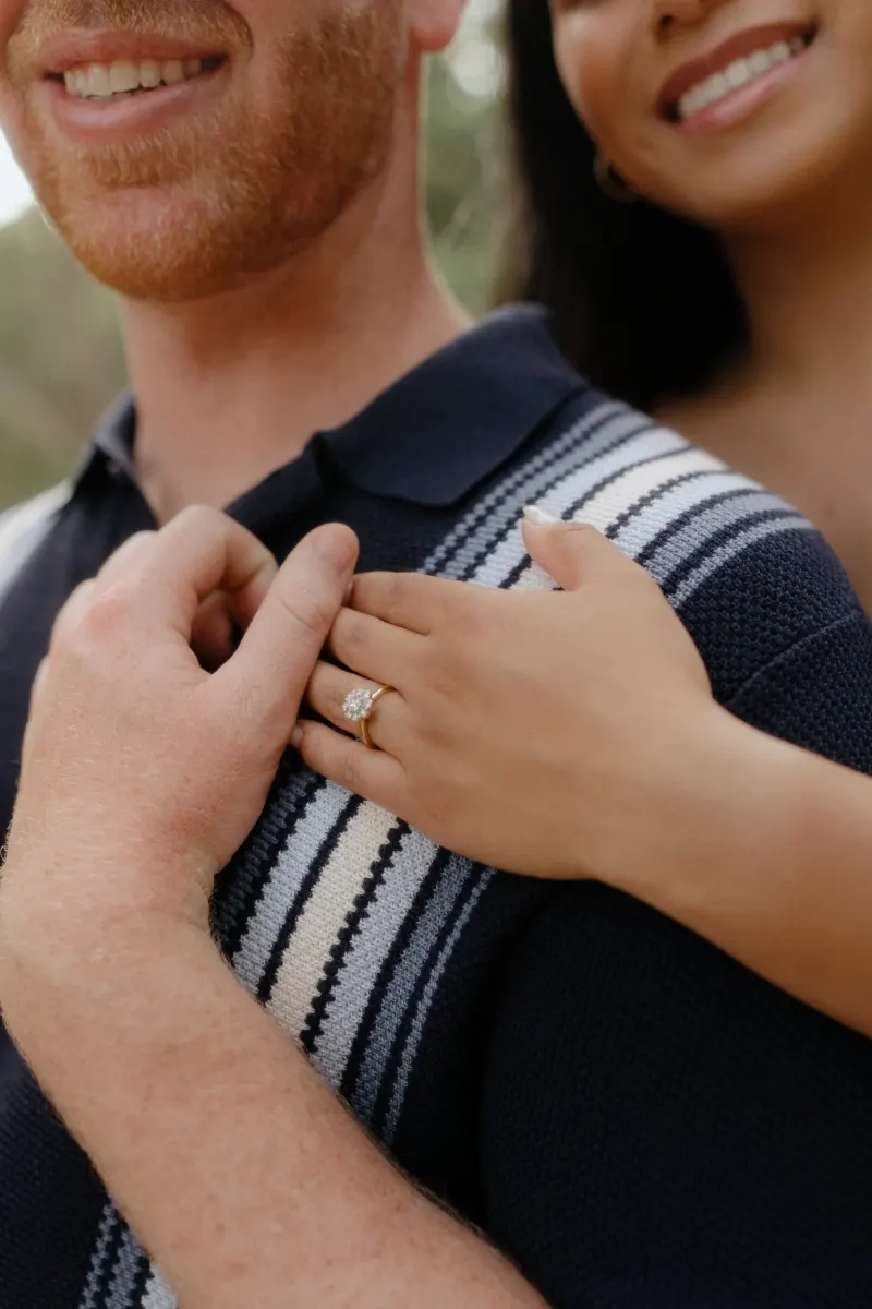 Close-up of newly engaged couple smiling as she shows off her ring during a surprise proposal photoshoot in the park.