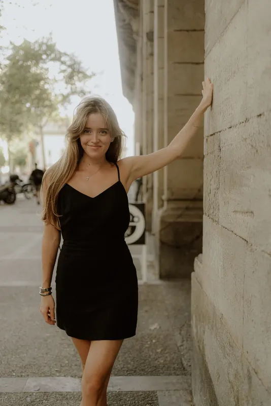 Confident woman in a black dress leans against a stone wall, enjoying a Vacation Portraits photoshoot in the city.