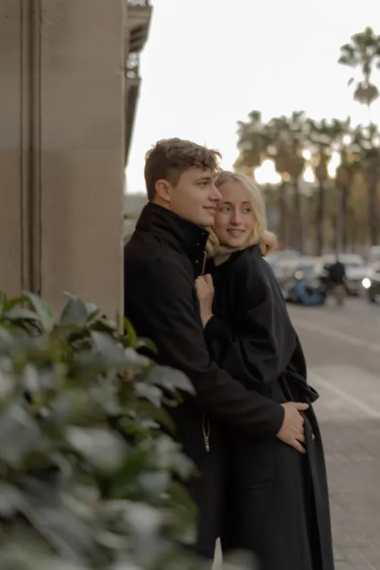 Couple cuddles warmly on a city sidewalk, sharing a quiet moment during a couples & engagements photoshoot in Barcelona.