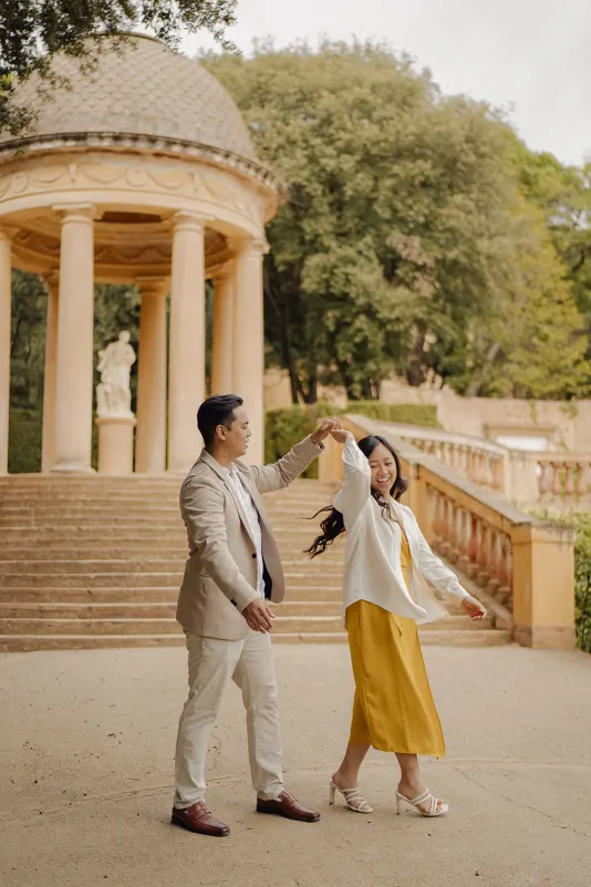 Couple dances and laughs together in front of a classical pavilion during a joyful couples & engagements photoshoot.