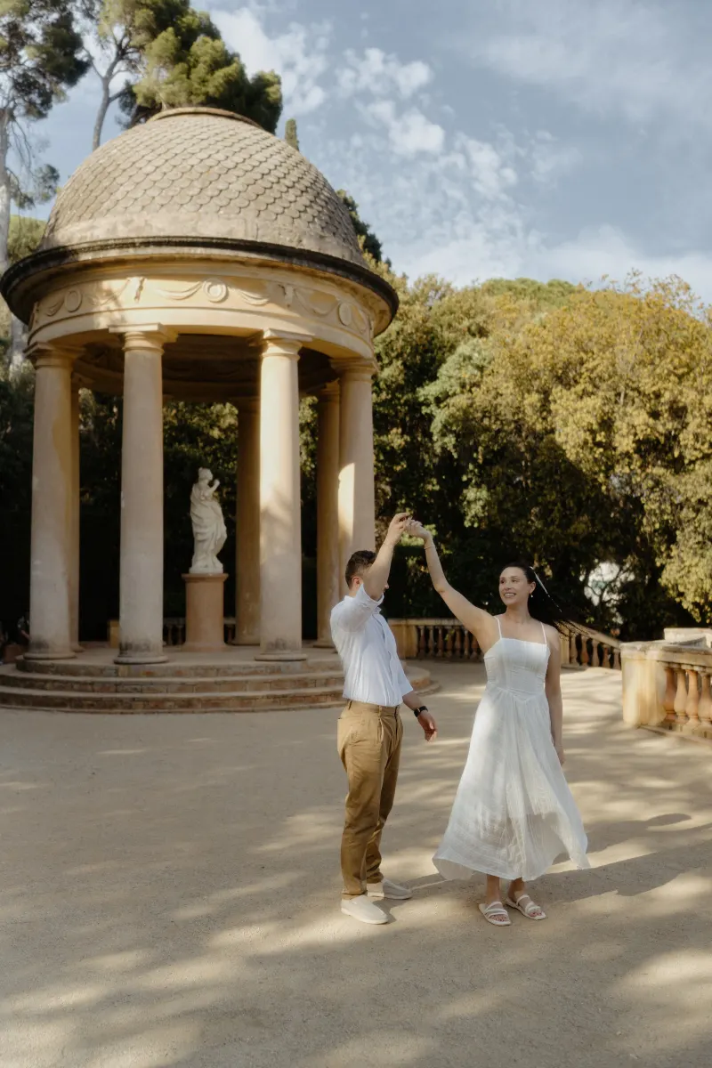 Couple dances joyfully in front of a classical pavilion, captured during a couples & engagements photoshoot in the garden.