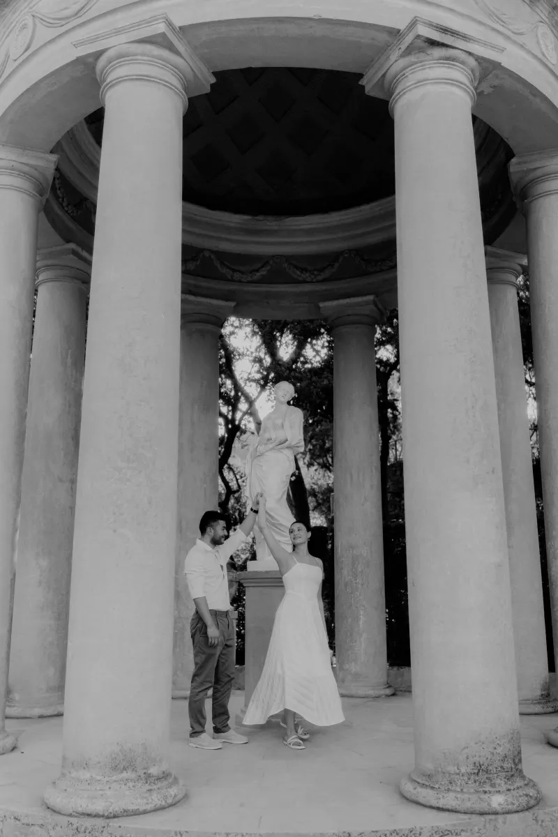 Couple dances together beneath a classical pavilion, sharing a romantic moment during an engagement photoshoot.