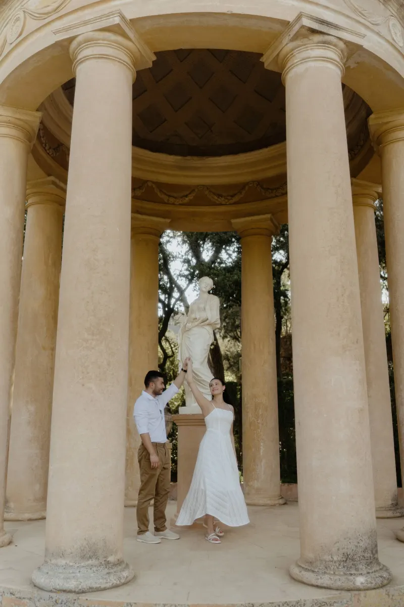 Couple dances together beneath a grand pavilion, sharing a joyful moment during a couples & engagements photoshoot.
