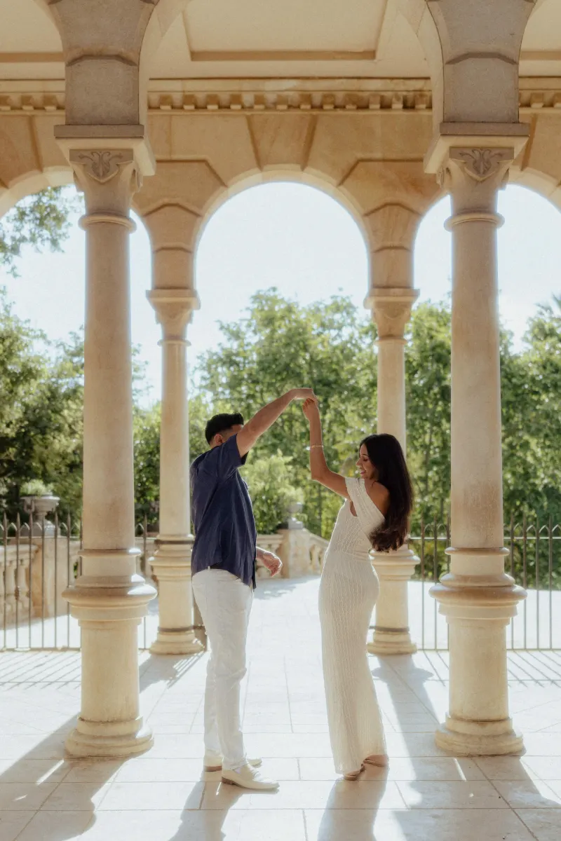 Couple dancing together under sunlit arches, sharing a joyful moment during a couples & engagements photoshoot.