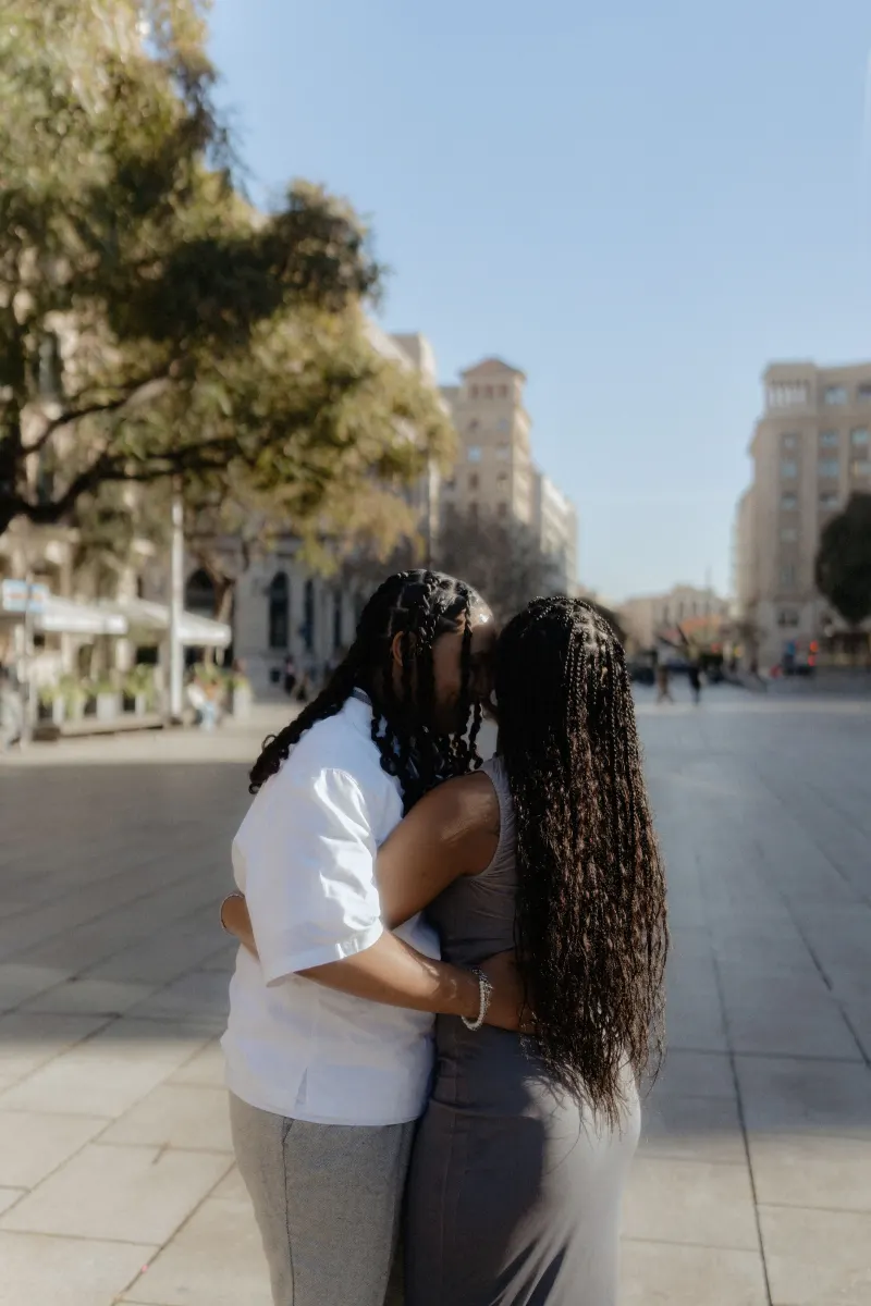 Couple embraces and kisses in the heart of Barcelona during a surprise proposal photoshoot, radiating happiness.