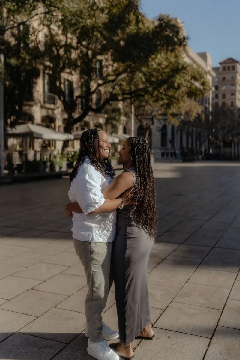 Couple embraces and laughs together in a sunlit plaza during a surprise proposal photoshoot in Barcelona.