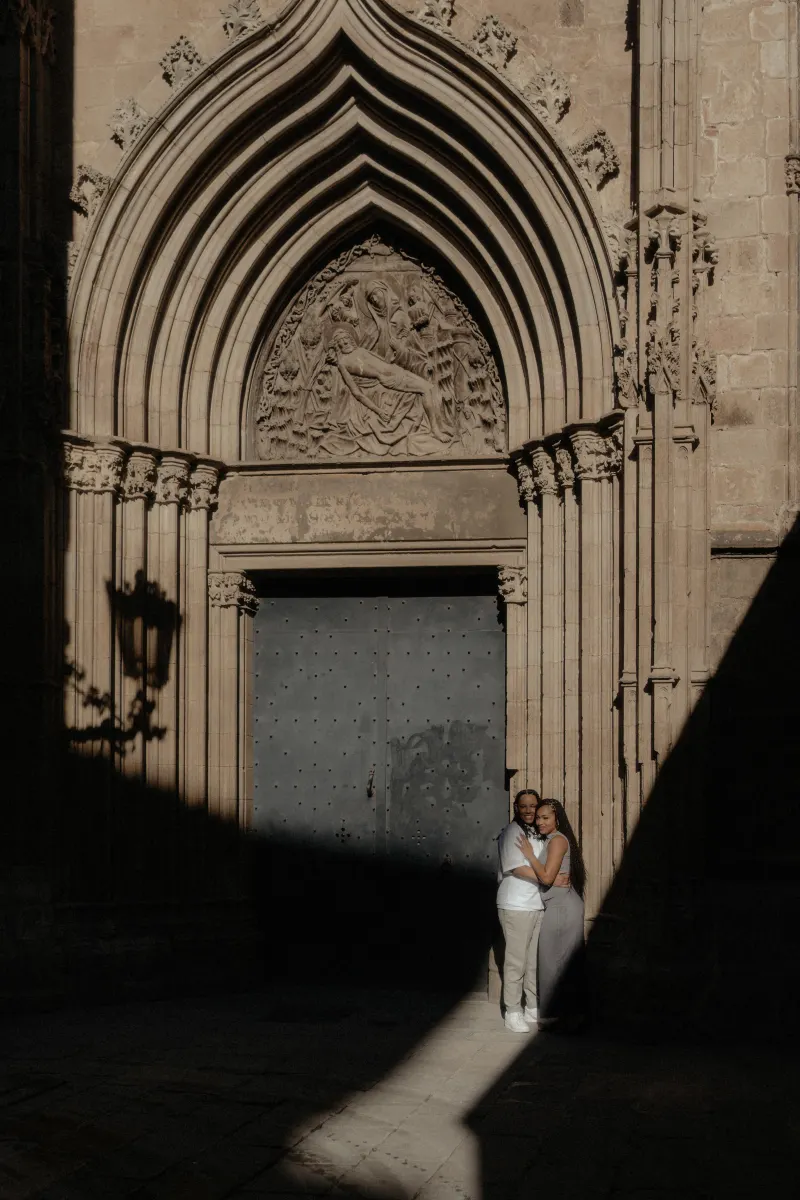 Couple embraces and smiles in a sunlit doorway of Barcelona Cathedral during their surprise proposal photoshoot.