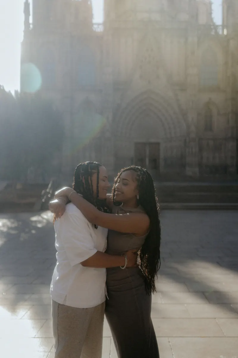 Couple embraces and smiles warmly after a surprise proposal in front of Barcelona Cathedral, captured in soft morning light.