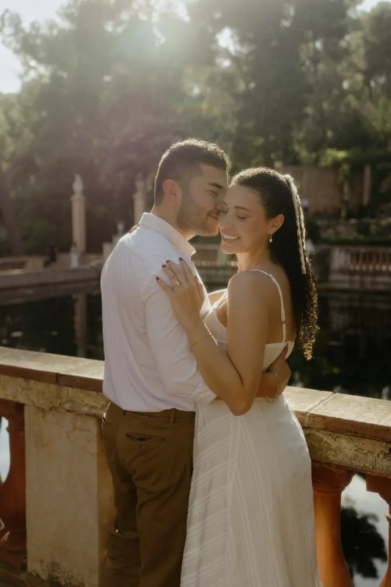 Couple embraces by a sunlit garden pond, sharing a joyful moment during their couples & engagements photoshoot.