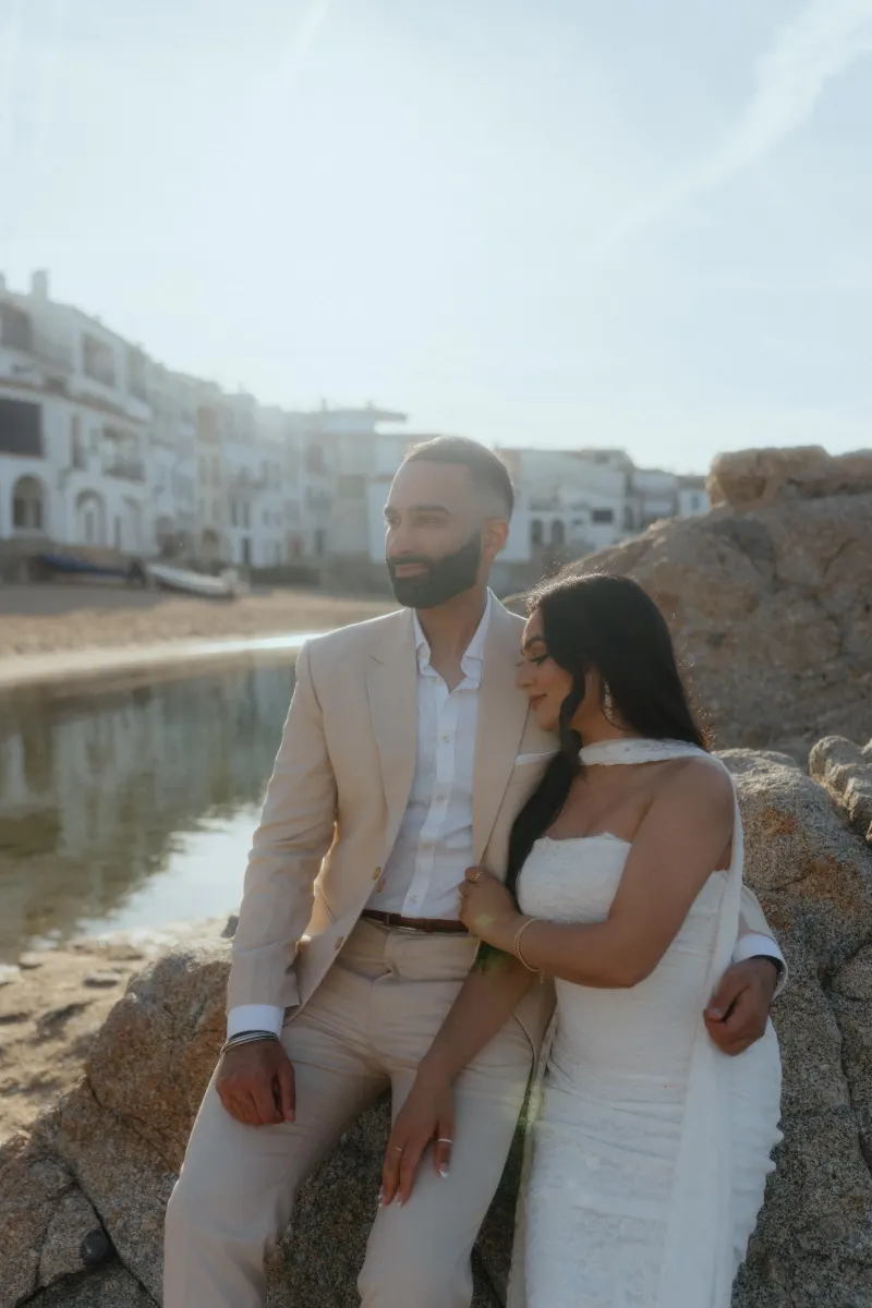 Couple embraces by the water at sunset during a surprise proposal photoshoot in a charming coastal village.