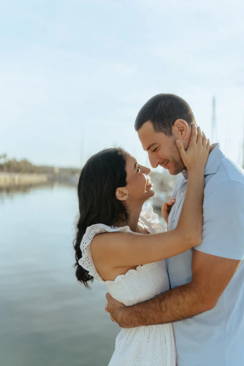 Couple embraces by the water, sharing a loving gaze during a couples & engagements photoshoot at the marina.