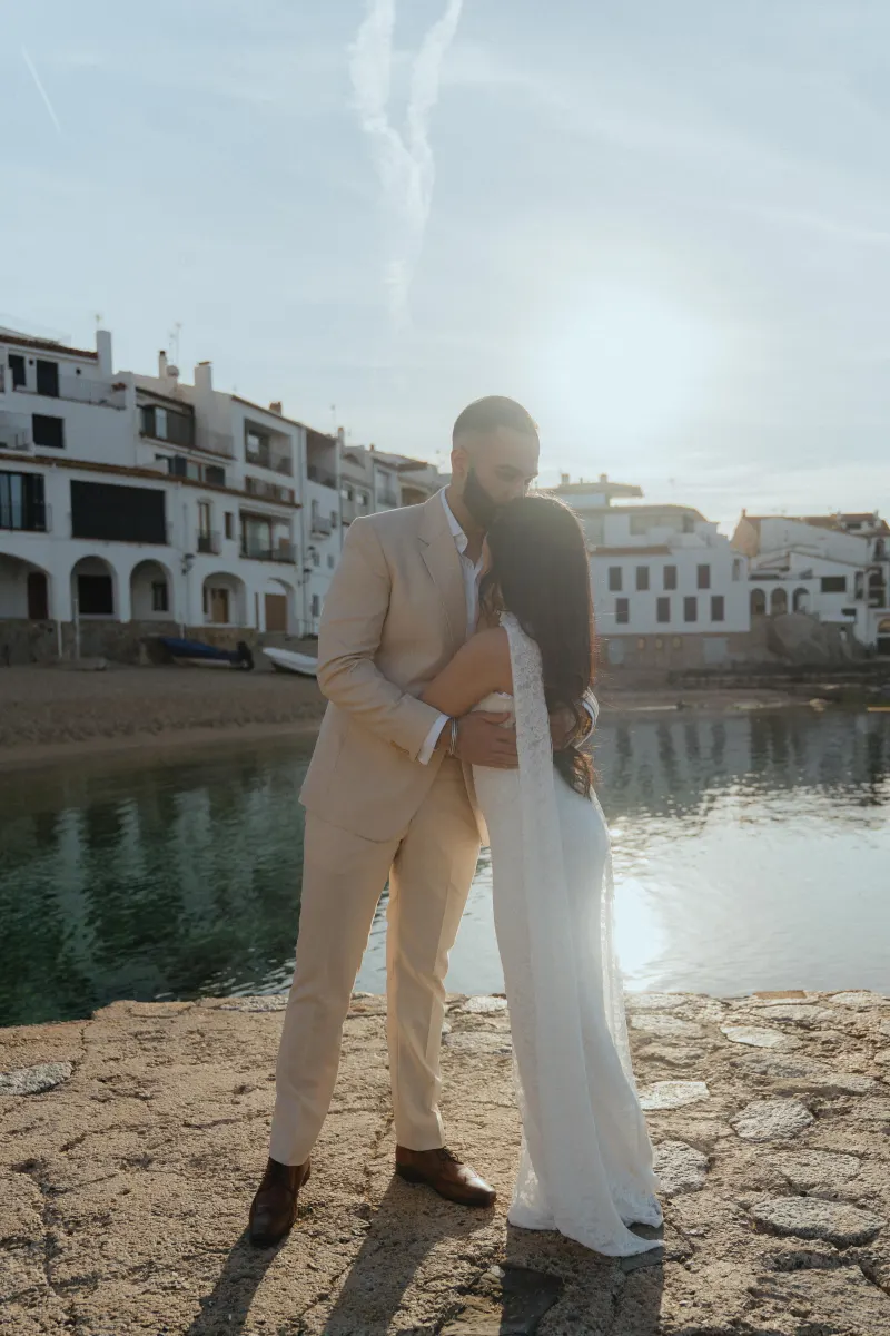 Couple embraces by the waterfront at sunset during a surprise proposal photoshoot in a charming coastal village.