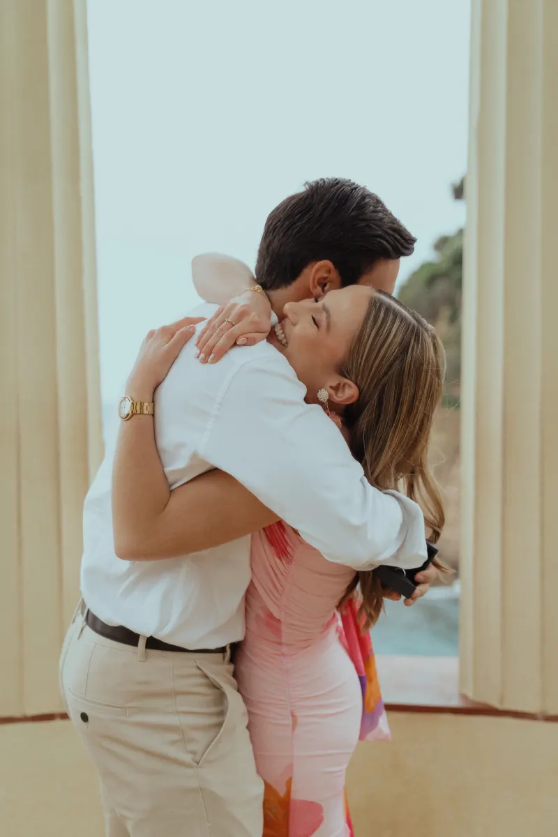 Couple embraces joyfully after a seaside proposal, captured during a surprise proposal photography session.
