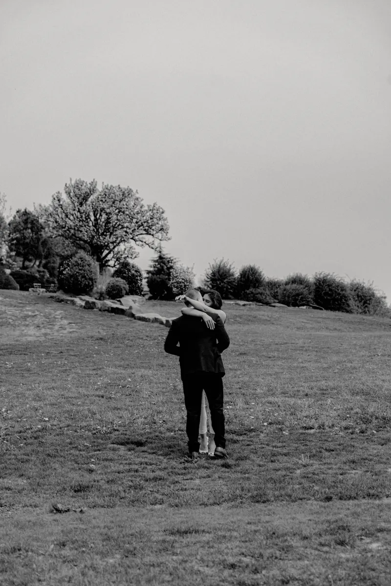 Couple embraces on a quiet hillside, sharing an emotional moment after a surprise proposal photoshoot in the countryside.