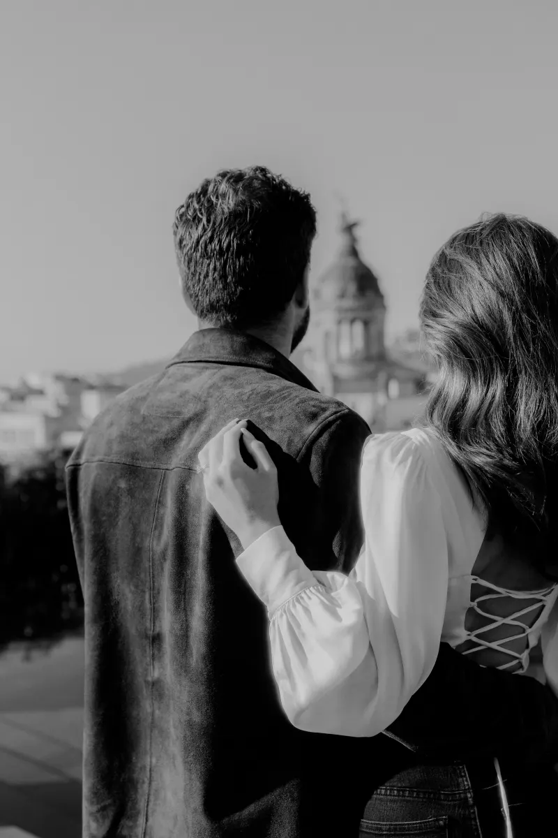 Couple embraces on a rooftop, gazing at city skyline during an engagement photoshoot.