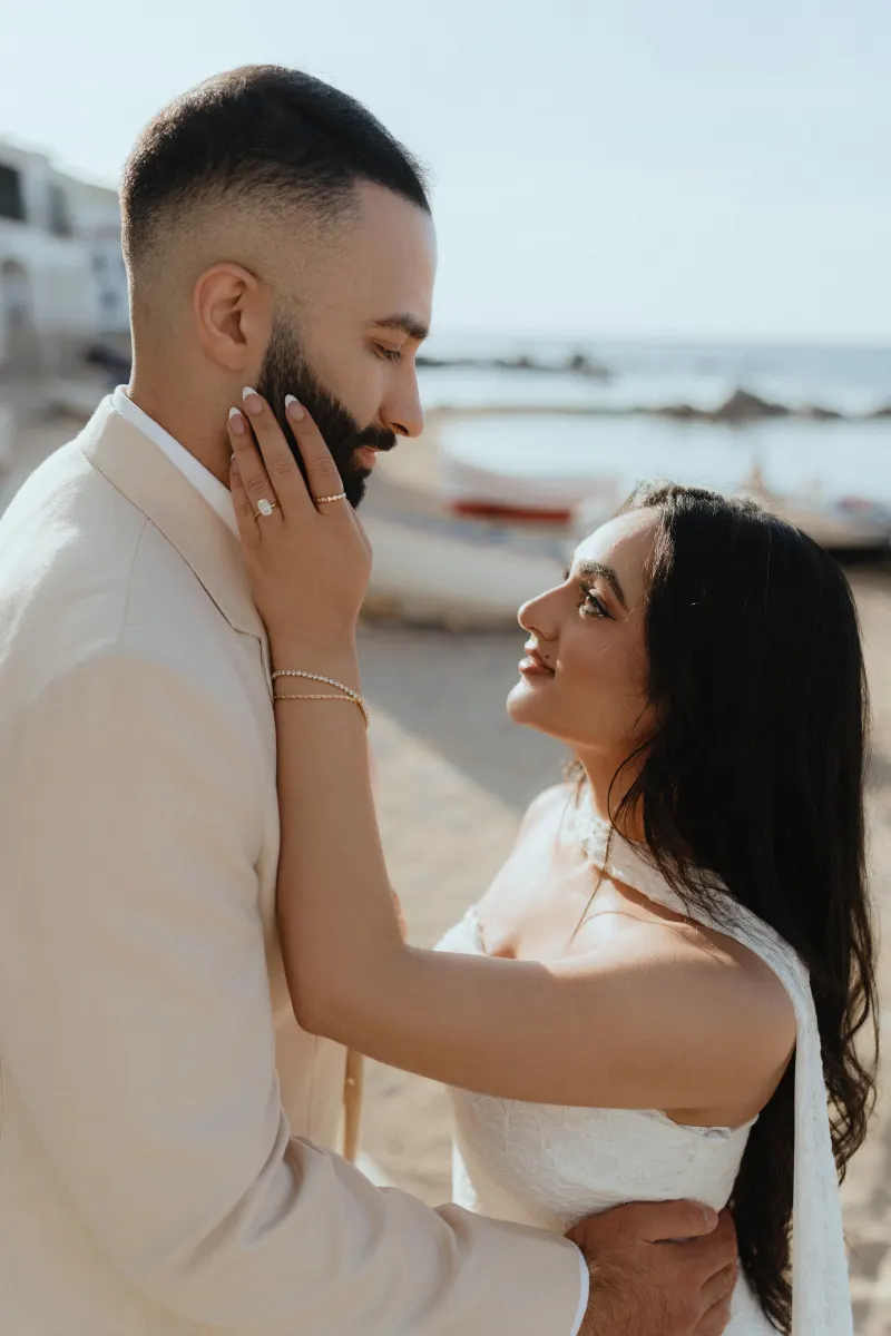 Couple embraces on a sunlit beach after a surprise proposal, capturing joy and intimacy in a candid photoshoot moment.